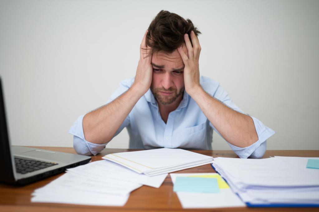 A man sitting at a desk looking stressed with papers.